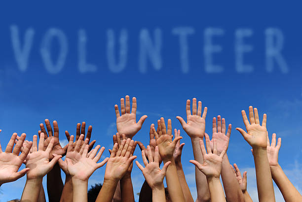 multi-ethnic volunteer group raising hands against blue sky